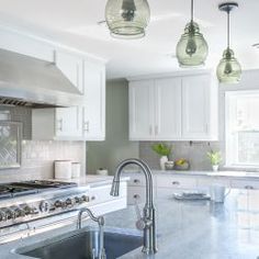 a kitchen with marble counter tops and white cabinets, hanging lights over the stove top