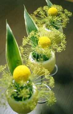 small vases with flowers and plants in them on a wooden table, ready to be used as centerpieces