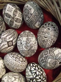 many decorated eggs in a wicker basket on a red tablecloth with black and white designs