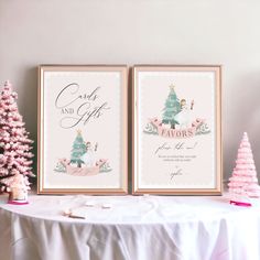 two framed christmas cards sitting on top of a table next to a small pink tree