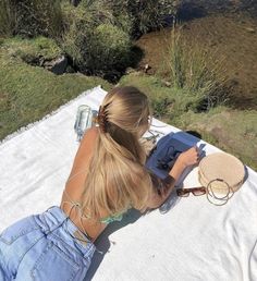 a woman sitting on top of a white blanket next to a river holding a straw hat