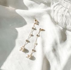 Exquisite and graceful dangle earrings that effortlessly harmonize with your feminine aesthetic. Complement your delicate white ensemble with these earrings to enhance your overall look. Ideal for both brides and those preparing to walk down the aisle. These stunning earrings combine lustrous gold-toned metal with the timeless elegance of faux pearls and the dazzling allure of faux diamonds. They strike the perfect balance between dainty and femininity. Comes with a pink dust bag for storage. White Jewelry For Everyday Elegance, Feminine Dangle Pearl Earrings For Formal Occasion, Feminine Formal Pearl Dangle Earrings, White Pearl Drop Clip-on Earrings For Wedding, White Drop Pearl Earrings For Everyday Elegance, Graceful Drop Earrings With Matching Set, Feminine Dangle Earrings For Formal Occasions, Elegant Pearl Dangle Chandelier Earrings, Elegant Pearl Chandelier Dangle Earrings