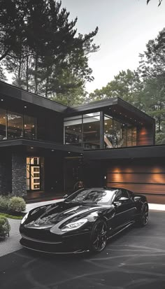 a black sports car is parked in front of a house with large windows and doors