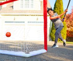 a young boy hitting a ball with a bat in front of a goalie net