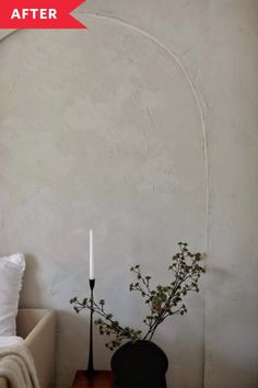 a living room with a white wall and a black vase filled with flowers on top of a table