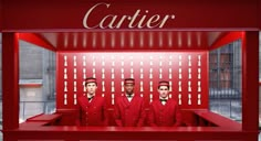 three men in red suits are standing behind a counter with the name cartier on it