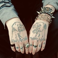 two hands with tattoos and rings on them