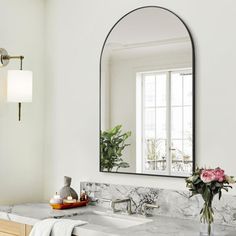 a bathroom with marble counter tops and a large oval mirror above the sink, along with a vase filled with flowers