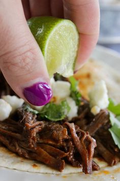 a hand is picking up a lime from a tortilla topped with shredded meat