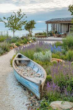 a boat sitting on top of a gravel road next to a lush green field filled with purple flowers