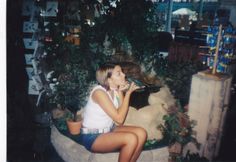 a young woman sitting on top of a plant filled area next to a bear statue