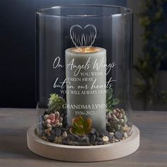 a memorial candle with succulents and rocks under a clear glass case on a wooden table