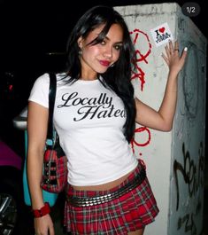 a woman in a white shirt and plaid skirt posing for the camera with her hand up