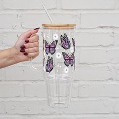 a hand holding a tumbler cup with butterflies on it and a straw sticking out of the lid