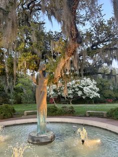 there is a statue in the middle of a fountain with water running through it and moss hanging from the trees