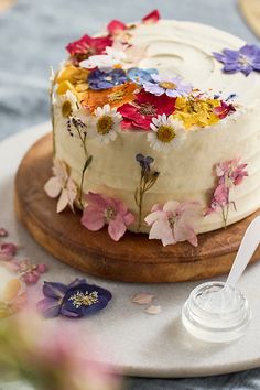 a cake with white frosting and colorful flowers on it sitting on a wooden platter