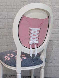 a white chair with pink and blue laces on it's back, sitting in front of a brick wall