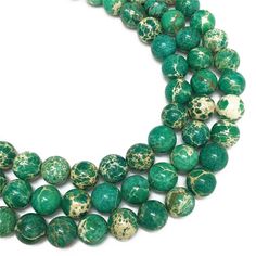 three strands of green and white marble beads on a white surface with gold speckles