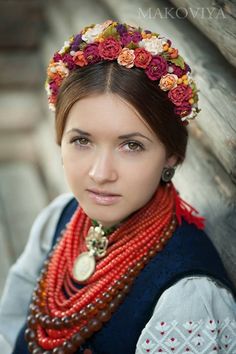 a woman wearing a flower headpiece and beads is posing for a photo in front of a wooden wall