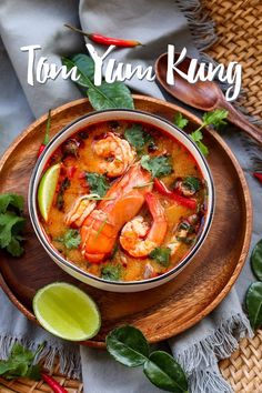 a bowl of soup with shrimp, lime and cilantro in it on a wooden plate