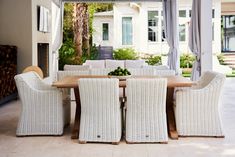 an outdoor dining area with white wicker chairs and a wooden table surrounded by curtains