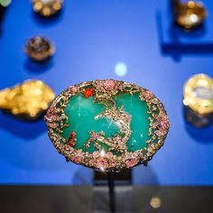 a green and gold brooch sitting on top of a black stand in front of blue walls