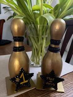 two gold bowling pins with black stars on them sitting next to a vase filled with green plants