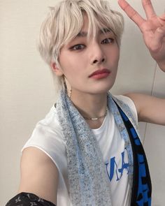 a young man with blonde hair wearing a white t - shirt and blue scarf holding his hand up in the air