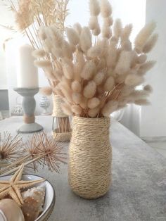 a vase filled with lots of dried plants on top of a table next to candles and seashells