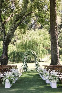 an outdoor ceremony set up with white flowers and greenery on the aisle, surrounded by trees