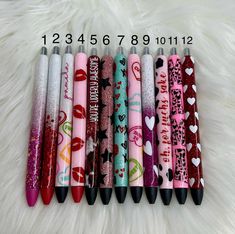 six pens with different designs are lined up on a white furnishing surface,