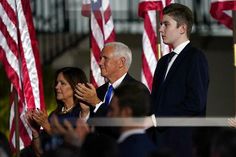 two men standing next to each other in front of american flags and people holding their hands up