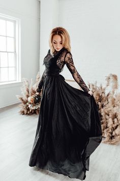 a woman in a long black dress standing on a wooden floor next to some plants