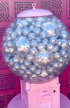 a pink machine with lots of shiny balls on it's top and bottom, sitting in front of a red wall