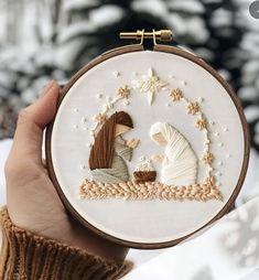 a person holding up a cross stitch hoop with a nativity scene in the middle