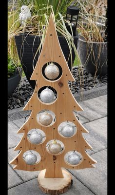 a wooden christmas tree with silver ornaments on it's sides and some potted plants in the background