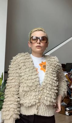 a woman with blonde hair and sunglasses standing in front of a stair case wearing a sweater