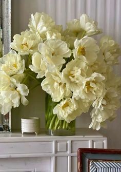 a vase filled with white flowers sitting on top of a table next to a mirror