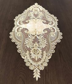 an intricately designed table cloth on top of a wooden table with white flowers and leaves