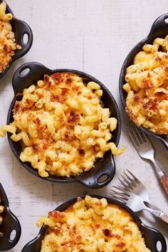 four cast iron skillets filled with macaroni and cheese on a white table