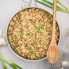 a pan filled with brown rice and green onions next to two wooden spoons on a gray surface