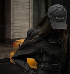 a woman wearing a black leather jacket and hat standing in front of a taxi cab