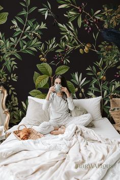 a woman sitting on a bed taking a selfie with her camera in front of a floral wallpaper