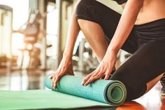 a woman rolling up a yoga mat on the floor with her hands and knees bent