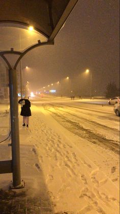 a person walking down a snow covered street at night with an umbrella over their head