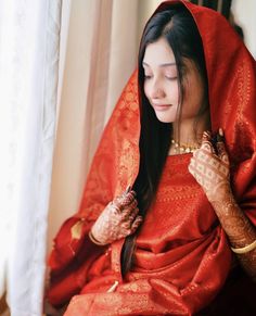 a woman with her hands on her face and wearing a red sari sitting in front of a window