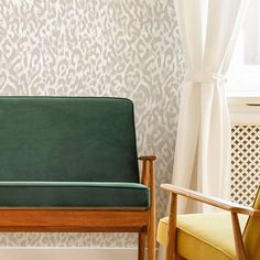 a green couch sitting in front of a window next to a wooden chair with yellow cushions