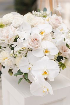 a bouquet of white and pink flowers sitting on top of a white box with greenery