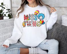 a woman sitting on a couch wearing a white sweatshirt with the word mom printed on it