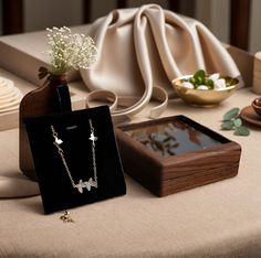 two necklaces and a box on a table with flowers in the vase next to it